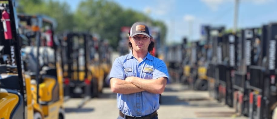 Learn more about working at Thompson Lift Truck - image of a Thompson Lift Truck employee standing in front of a range of forklift machines.