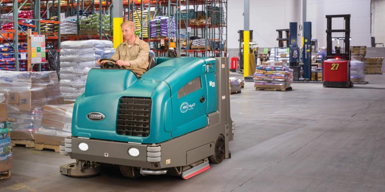 Tennant M20 ride-on floor scrubber in a warehouse, efficiently cleaning large areas with advanced features. Available at Thompson Lift Truck for your commercial cleaning needs.