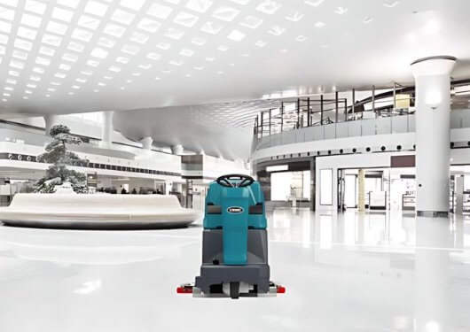 Tennant ride-on floor scrubber in a modern commercial space, ensuring spotless floors with EC-H2O technology. Available at Thompson Lift Truck for efficient cleaning.