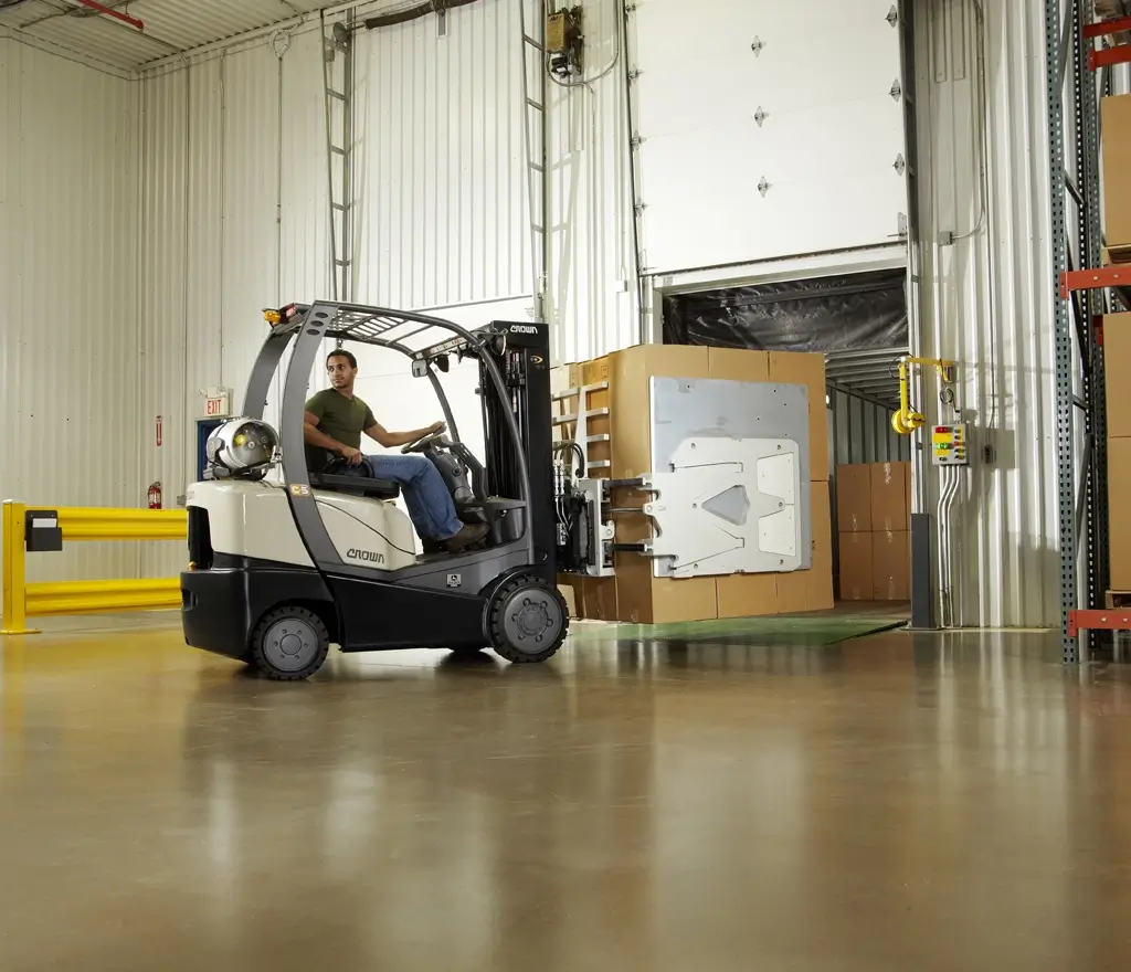 Operator driving a Crown forklift with clamp attachment at a warehouse loading dock, featured in Thompson Lift Truck’s Crown forklift guide