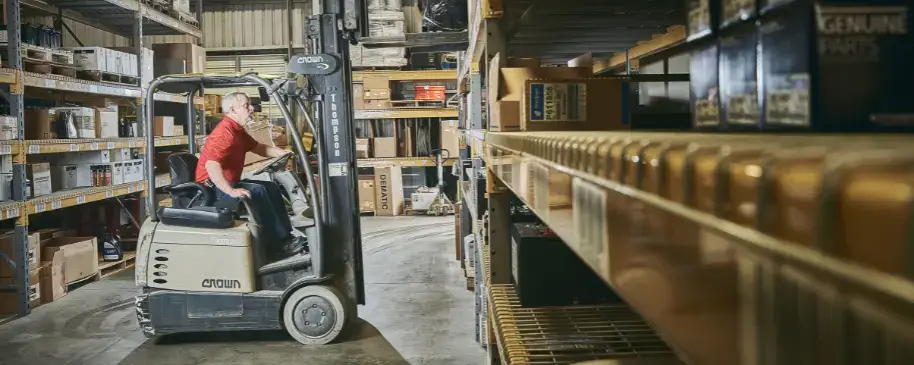 Forklift operator driving through warehouse aisle at Thompson Lift Truck, trusted forklift dealer and parts provider in the Southeast