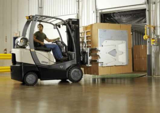 An operator uses a Crown forklift with a carton clamp attachment to move a large box inside a clean Alabama warehouse, near a loading dock