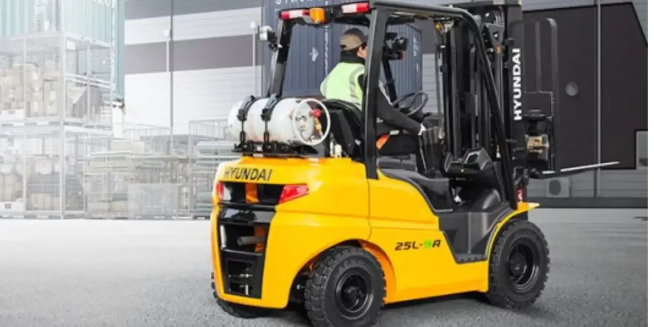 A side view of a yellow Hyundai 25L-9A forklift, a popular model for warehouses and businesses across Alabama, with a driver in a safety vest at the controls