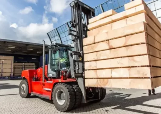 A heavy-duty red forklift rented from Thompson Lift Truck lifting a large stack of lumber in an industrial yard Georgia