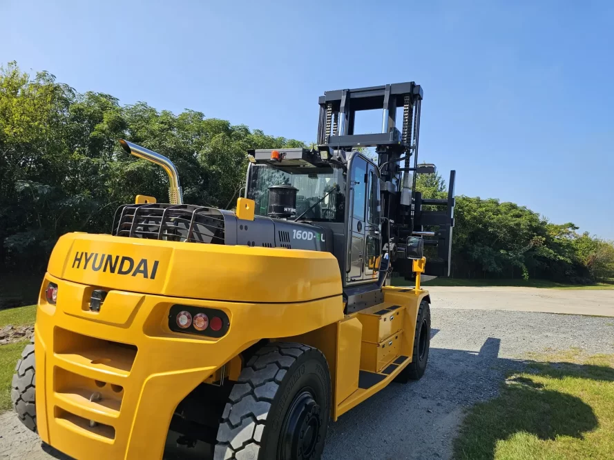 A large, yellow Thomspon Lift Truck parked outdoors on a sunny day, with green trees in the background.